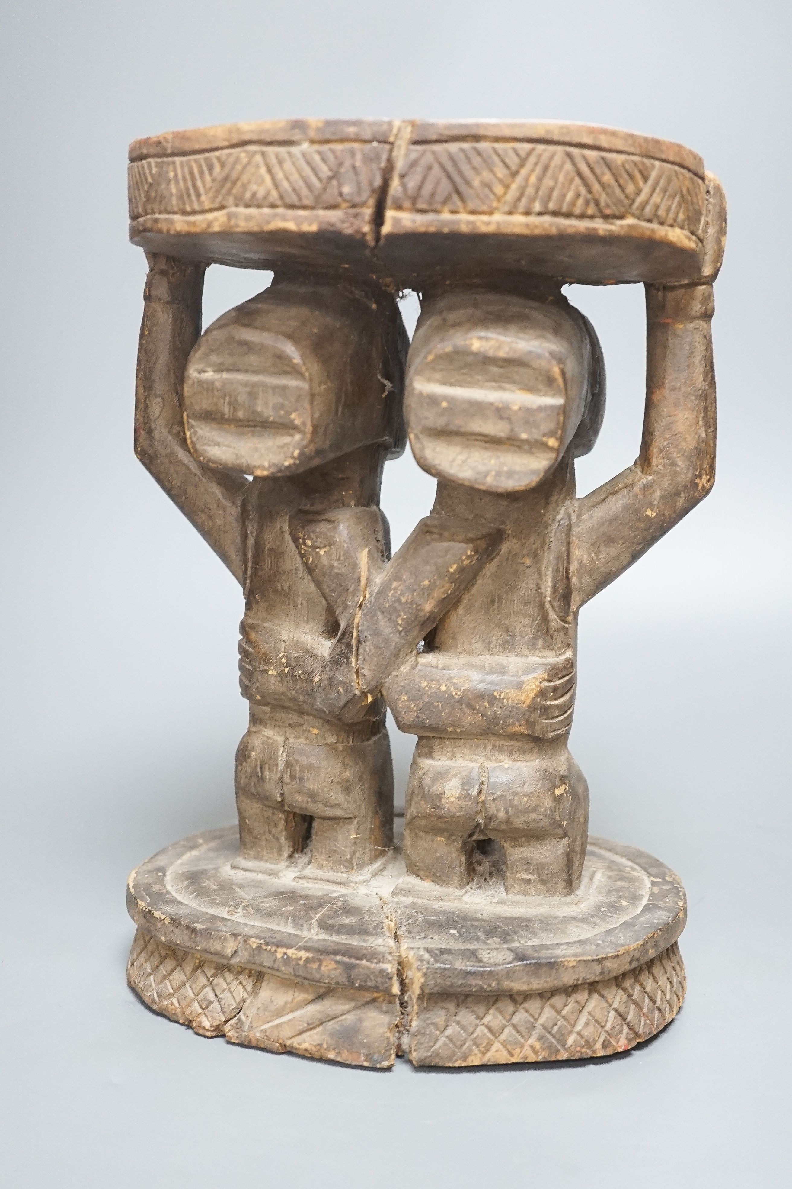 A Yoruba carved wood stool, modelled with male and female figures 27cm